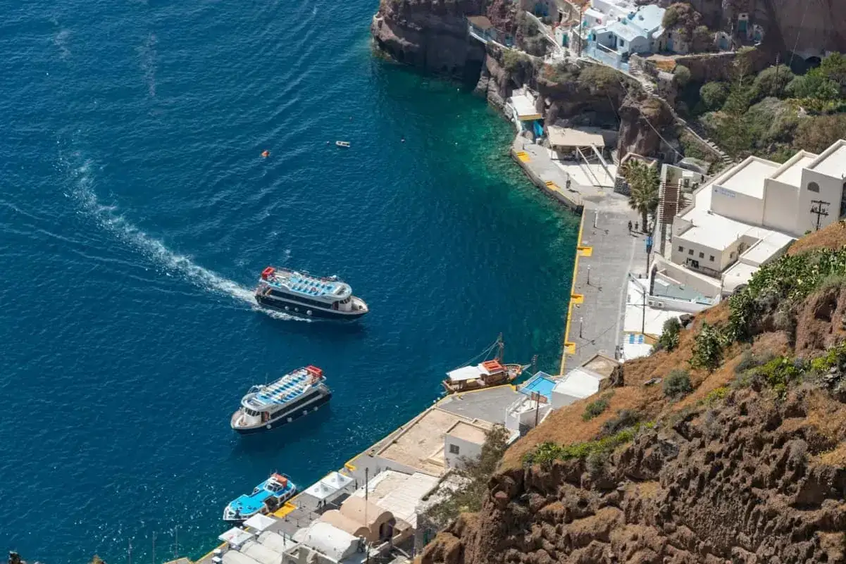 Barche turistiche navigano nel blu intenso del porto di Santorini, con le case bianche aggrappate alla scogliera.