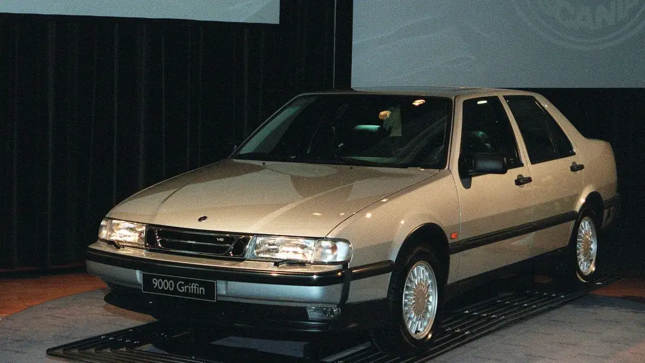 En ljusbeige Saab 9000 Griffin, en klassisk 90 tals bil, står upplyst på en mässa.