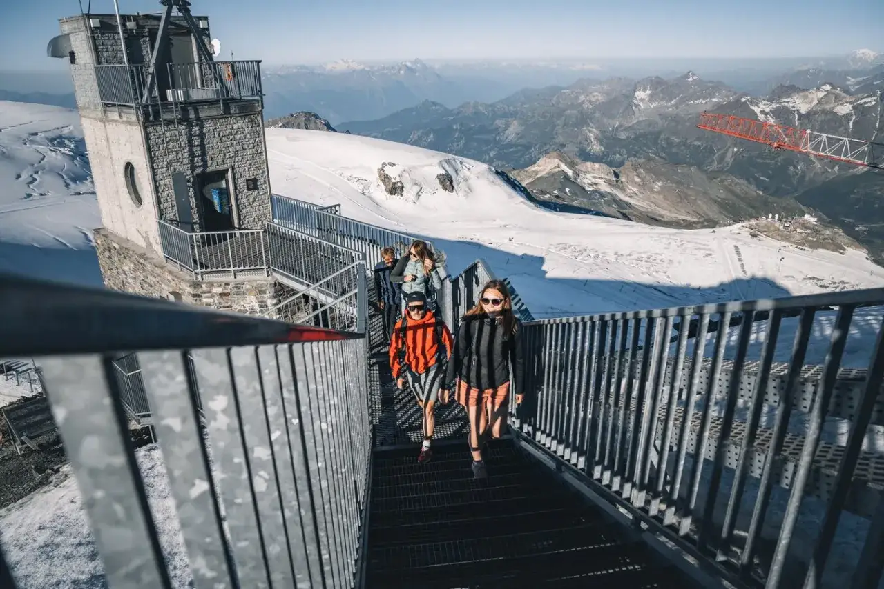 Menschen steigen eine Treppe hinauf, mit Blick auf schneebedeckte Berge und den Matterhorn Gipfel in der Ferne.