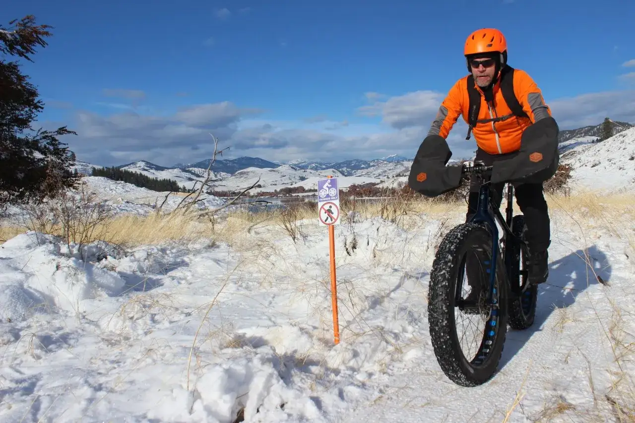 Mann f&auml;hrt mit einem Fatbike durch verschneite Landschaft. Das Schild sagt 