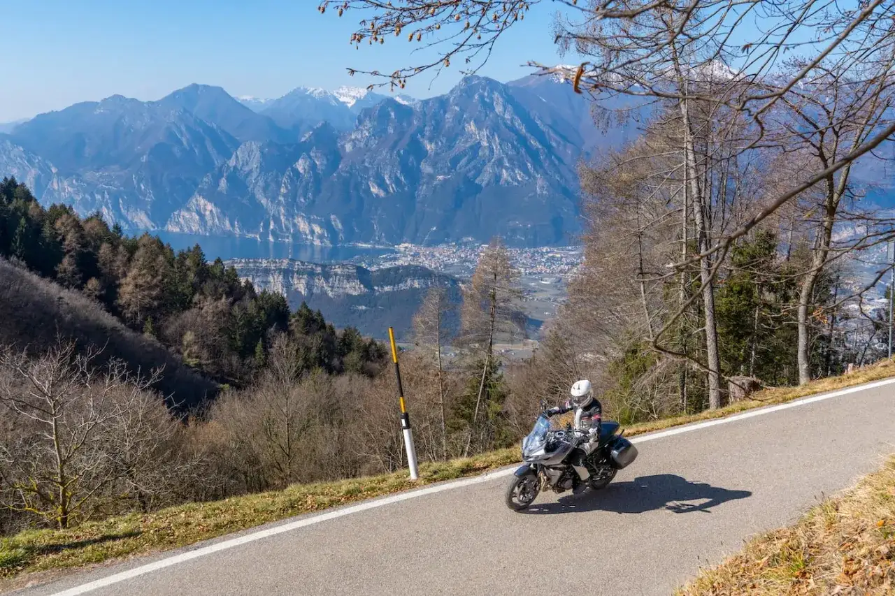 Motociclista in discesa panoramica, con il Lago di Garda e le montagne sullo sfondo. Un viaggio indimenticabile rund um den Gardasee.