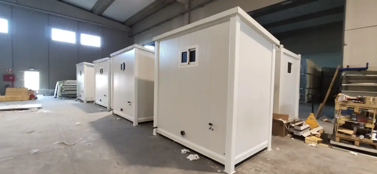 Varias cabinas de ba&ntilde;o prefabricadas blancas, listas para su instalaci&oacute;n, se alinean en un almac&eacute;n.