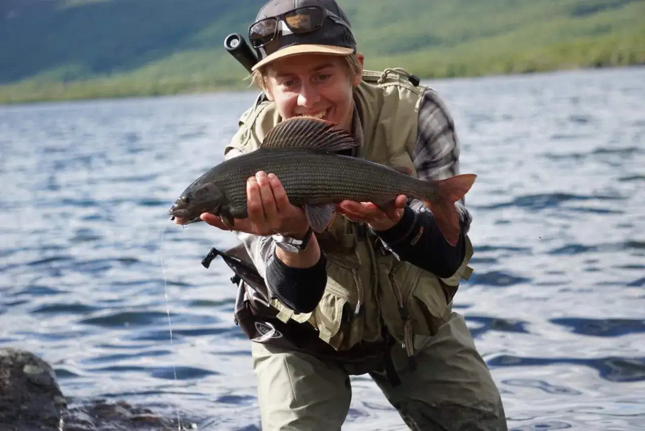 Lycklig fiskare håller upp en fin harr efter en lyckad **trout fishing**-tur vid en sjö.