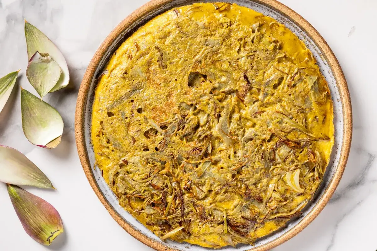 Frittata di carciofi dorata e invitante, con carciofi sfilacciati e cipolla caramellata, servita in un piatto rustico.