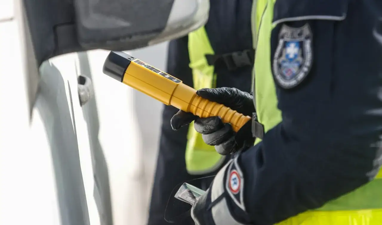 Policjant w rękawiczkach trzyma żółty alkomat, gotowy do badania kierowcy. Czy pracownik ochrony może badać alkomatem? To pytanie często zadawane przez kierowców.