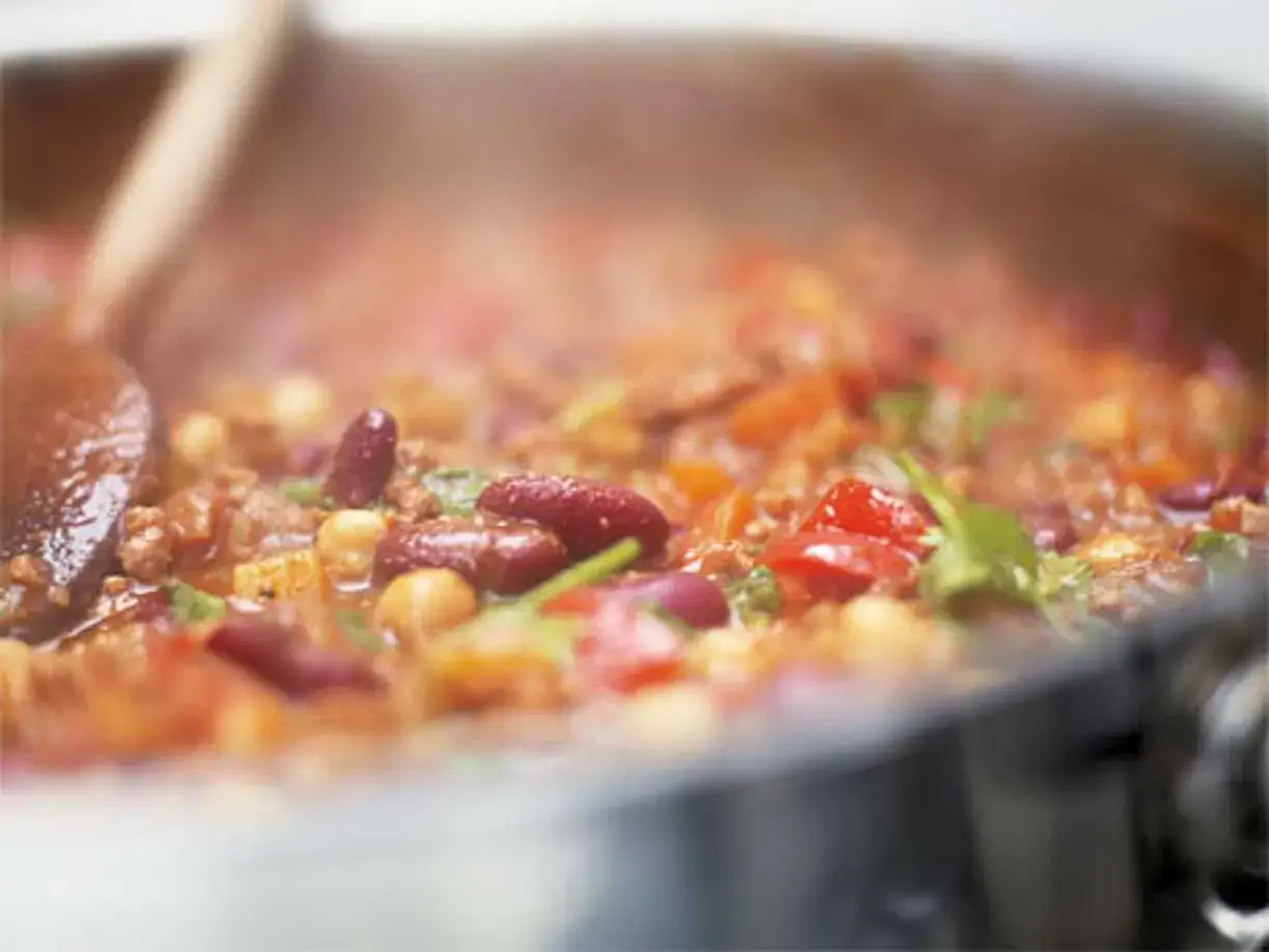 En varm och ångande gryta med chili con carne, full av bönor, köttfärs och grönsaker. En träsked rör om i den mustiga rätten.