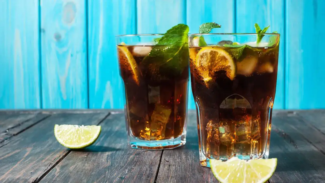 Dwa orzeźwiające drinki z rumem, z lodem, cytryną i miętą, na drewnianym stole. Idealne na upalne dni.