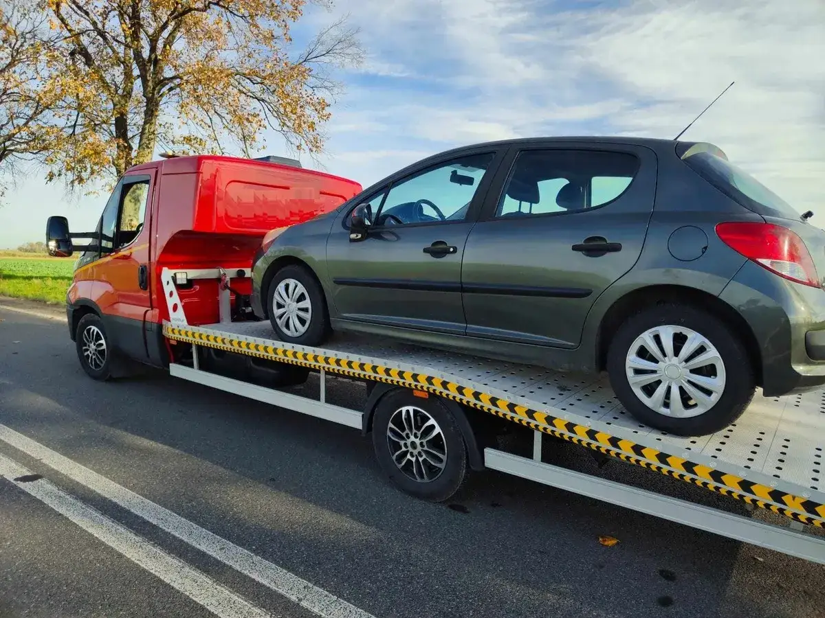 Pomarańczowy laweta z szarym samochodem na platformie. Konfiskata samochodu w drodze na złomowisko.