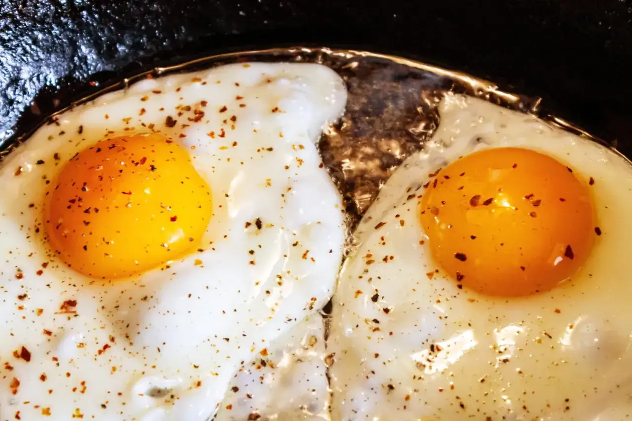 Deux &oelig;ufs au plat cuisent dans une po&ecirc;le, leurs jaunes brillants et leurs blancs fondants. Un aper&ccedil;u de comment faire des oeufs au plat.