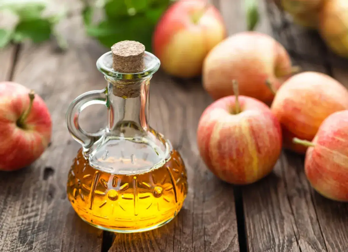 Szklana buteleczka z płynem i jabłka na drewnianym stole. Czy wiesz, oxymel co to? To naturalny syrop z octu jabłkowego i miodu.