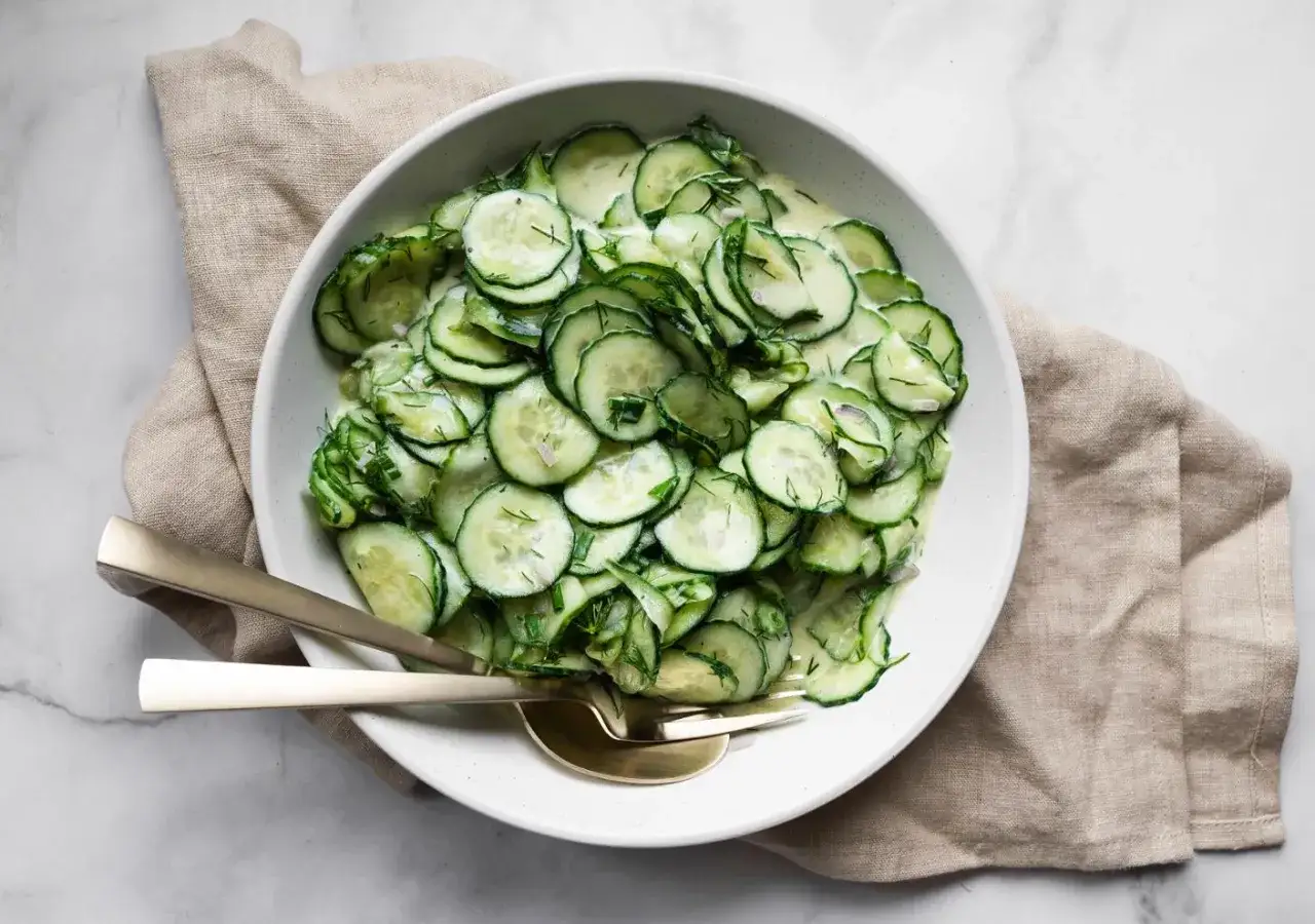 Frischer, cremiger Gurkensalat mit Dill und Zwiebeln, der beste Gurkensalat für heiße Tage. Serviert mit goldenem Besteck.