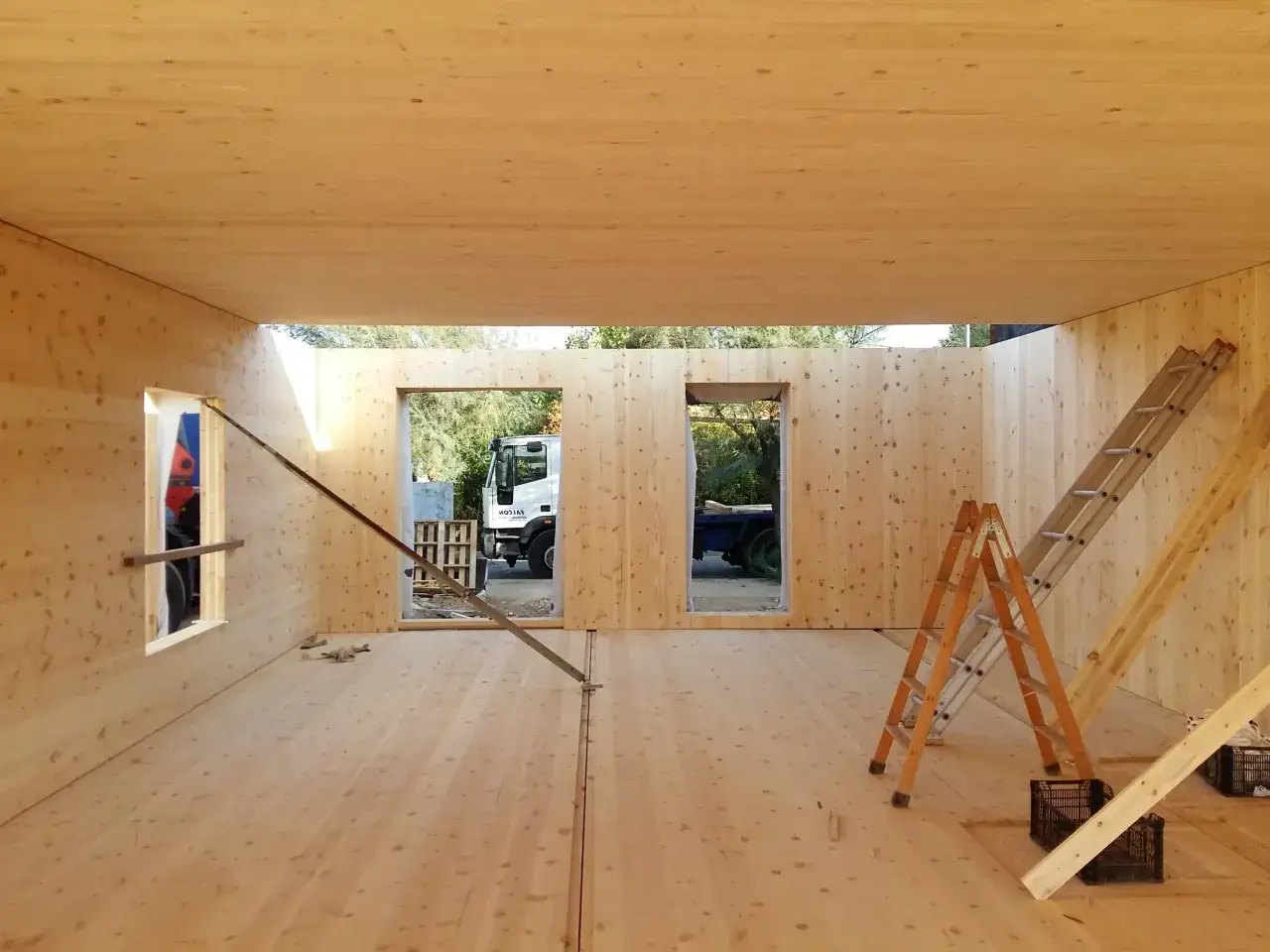 Interior de una casa en construcci&oacute;n con estructuras de madera. Se ven escaleras y una carretilla elevadora al fondo.