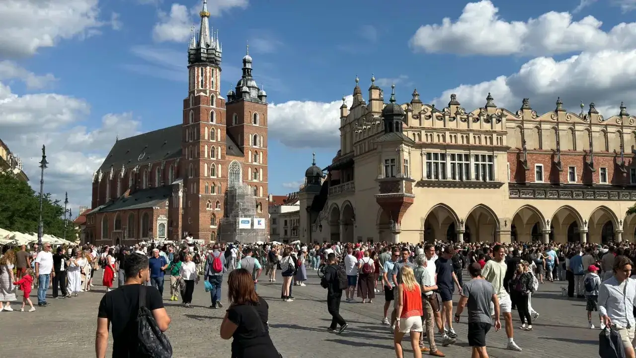 Tłum ludzi na Rynku Głównym w Krakowie, podziwiający architekturę. Czy Polska jest bezpieczna? Tak, turyści czują się tu swobodnie.