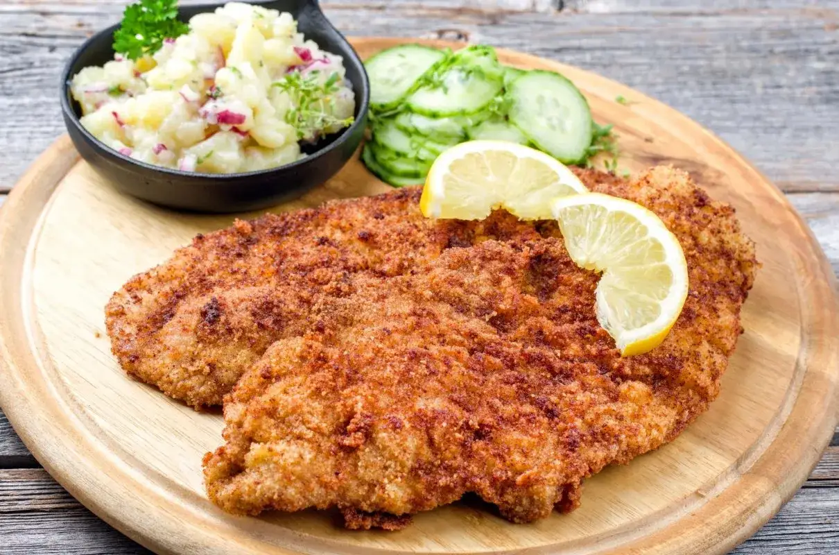Złocisty kotlet schabowy z cytryną, obok sałatka ziemniaczana i ogórek. Pyszny obiad, warto sprawdzić kotlet schabowy kcal.