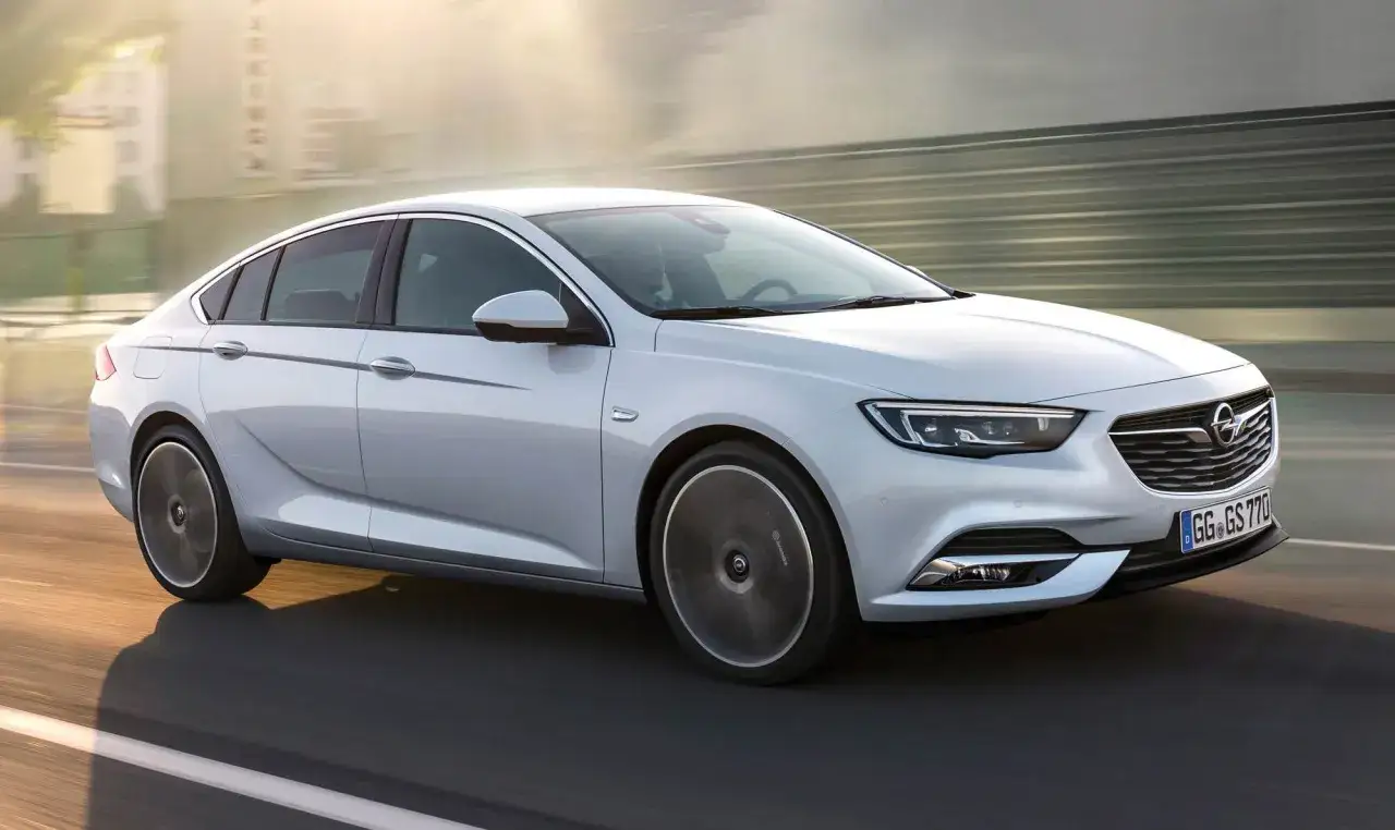 En vit Opel Insignia glider fram p&aring; en v&auml;g i solnedg&aring;ngen, med en k&auml;nsla av fart och elegans.