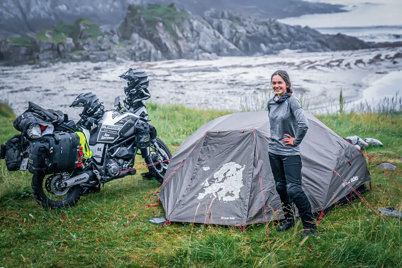 Kobieta pozuje przy namiocie z mapą Europy i motocyklem wyprawowym. To idealne miejsce na **Nordcamp Norwegia**.