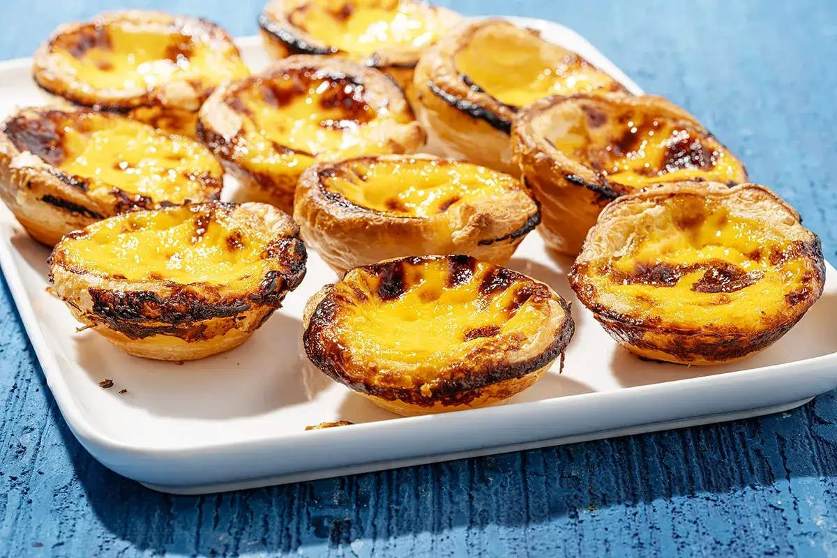 Un vassoio pieno di deliziosi pastel de nata, con la loro crosta sfogliata e il ripieno cremoso e caramellato.