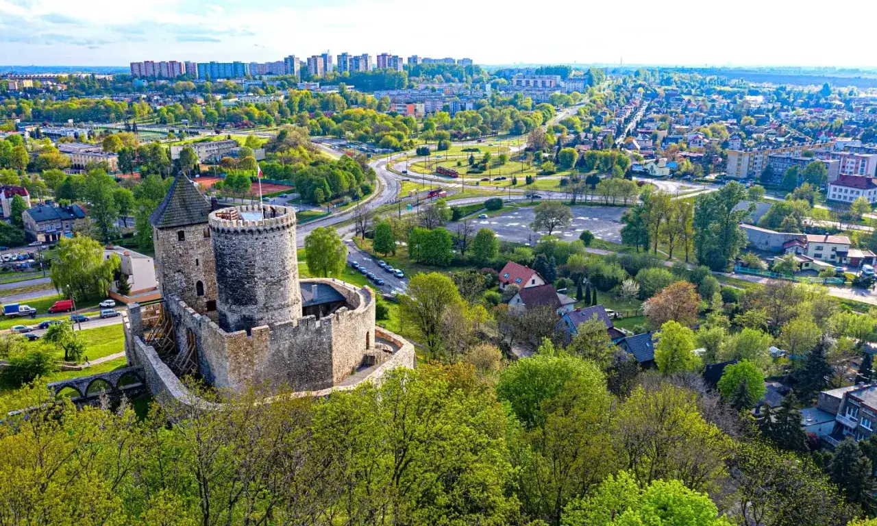 Kamienny zamek g&oacute;ruje nad miastem, przypominając o historii zamk&oacute;w na Śląsku. W tle widać zabudowania i zieleń.