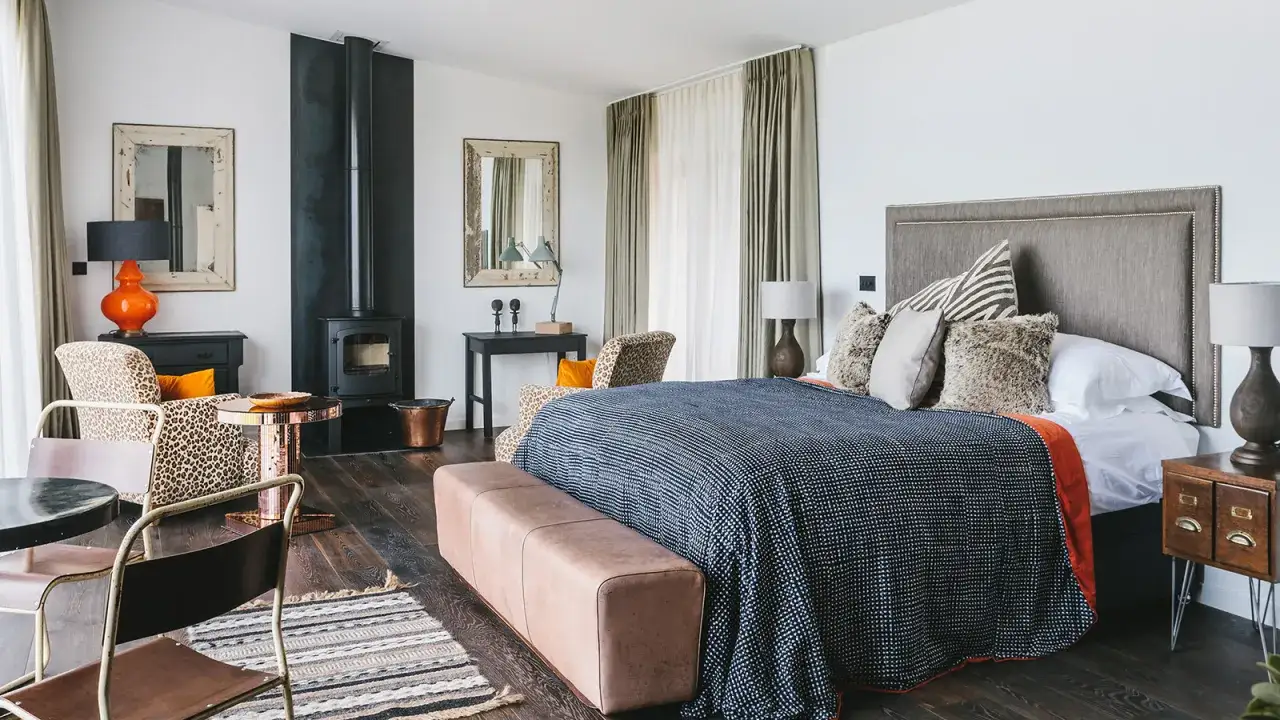 Stylish bedroom with a wood-burning stove, leopard-print chairs, and a tufted headboard. This image offers inspiration on how to pick bedroom furniture for a chic, eclectic look.
