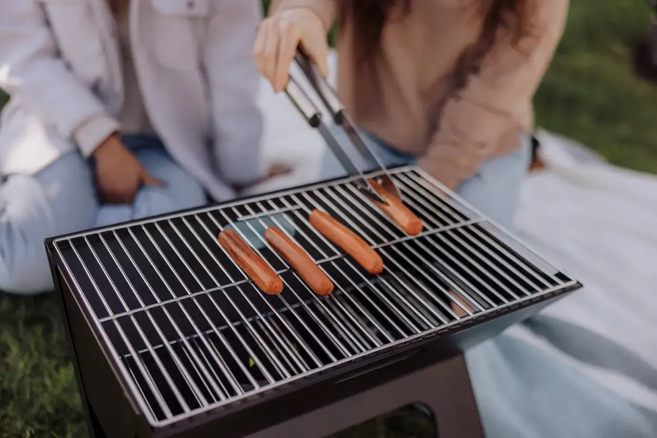 Personer grillar korv p&aring; en b&auml;rbar kolgrill utomhus.