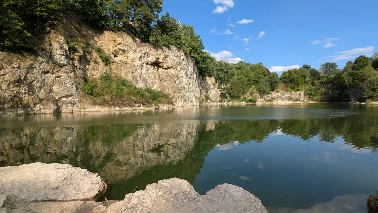 Spokojny zalew kamieniołom w Zabierzowie, z odbijającymi się w wodzie skalnymi ścianami i zielenią drzew.