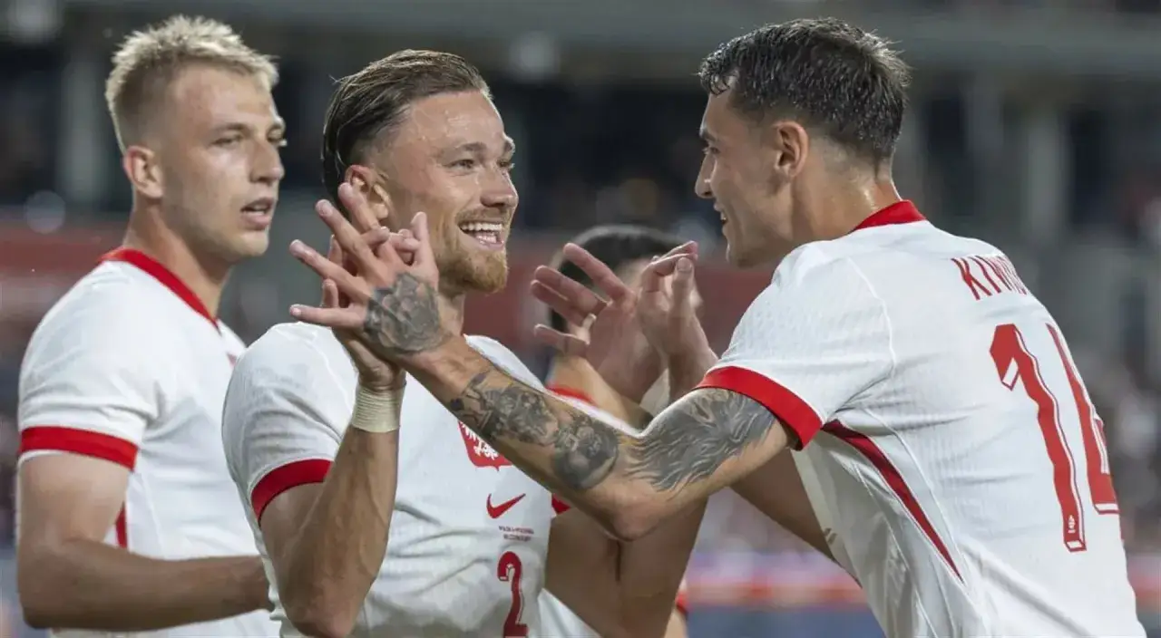 Piłkarze reprezentacji Polski w białych strojach świętują bramkę. Uśmiechnięty zawodnik z tatuażami na ramieniu cieszy się z kolegą z drużyny. Duma z barw narodowych.