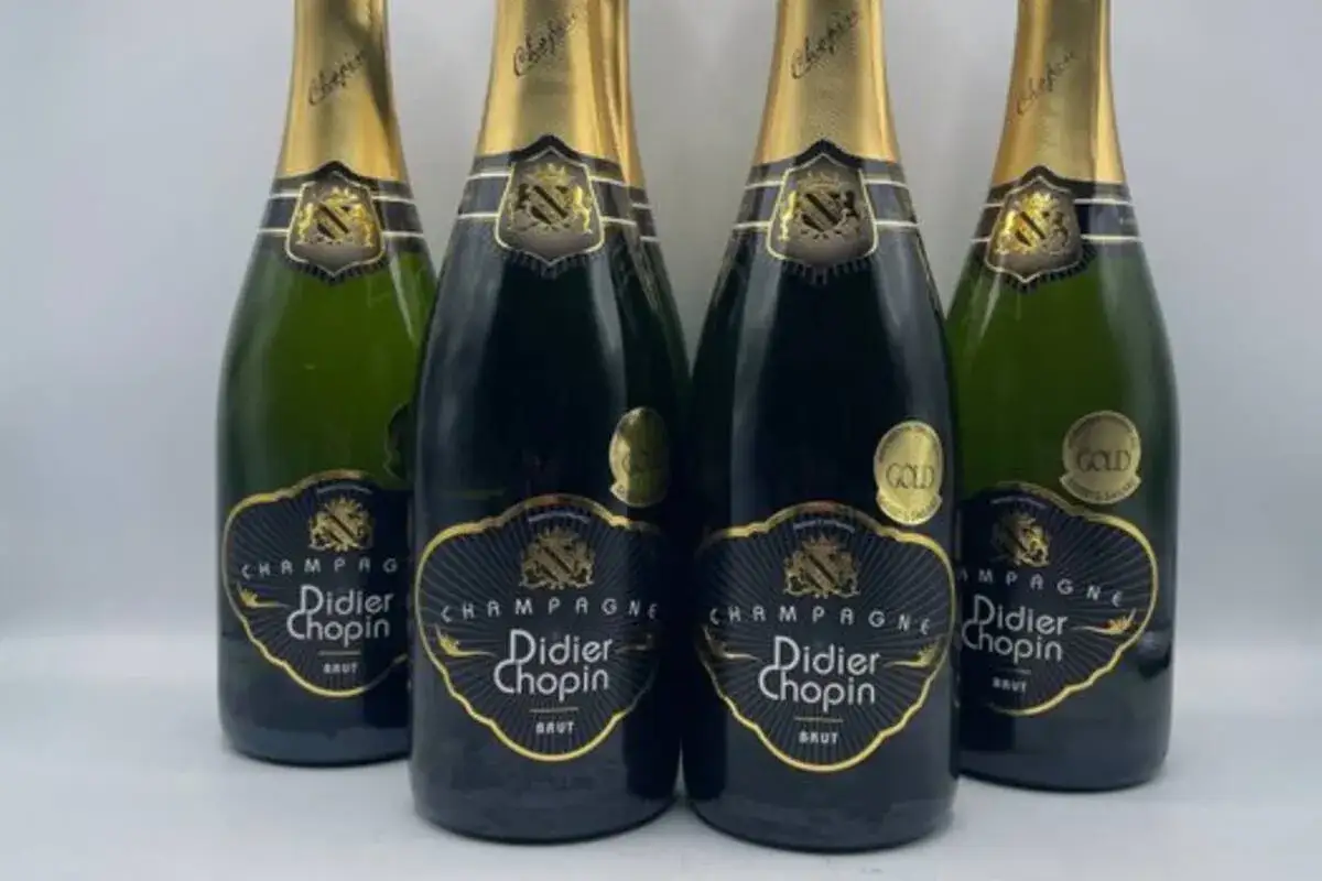 Quatre bouteilles de champagne Didier Chopin Brut, avec leurs étiquettes noires et dorées. Un avis sur ce champagne est attendu.