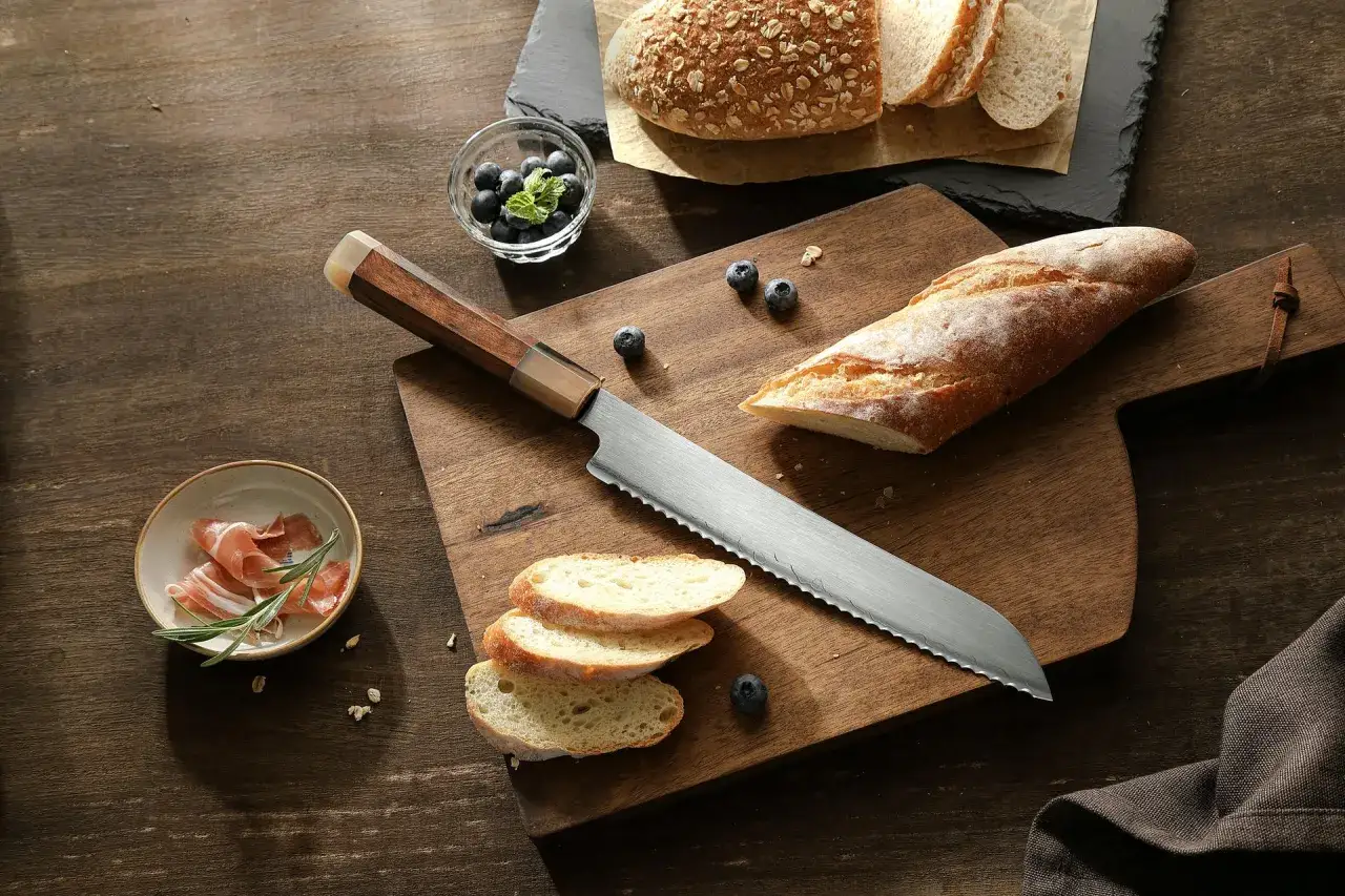 N&oacute;ż do chleba z ząbkowanym ostrzem leży obok świeżego pieczywa, jag&oacute;d i prosciutto. Zastanawiasz się, dlaczego chleb się klei do noża?