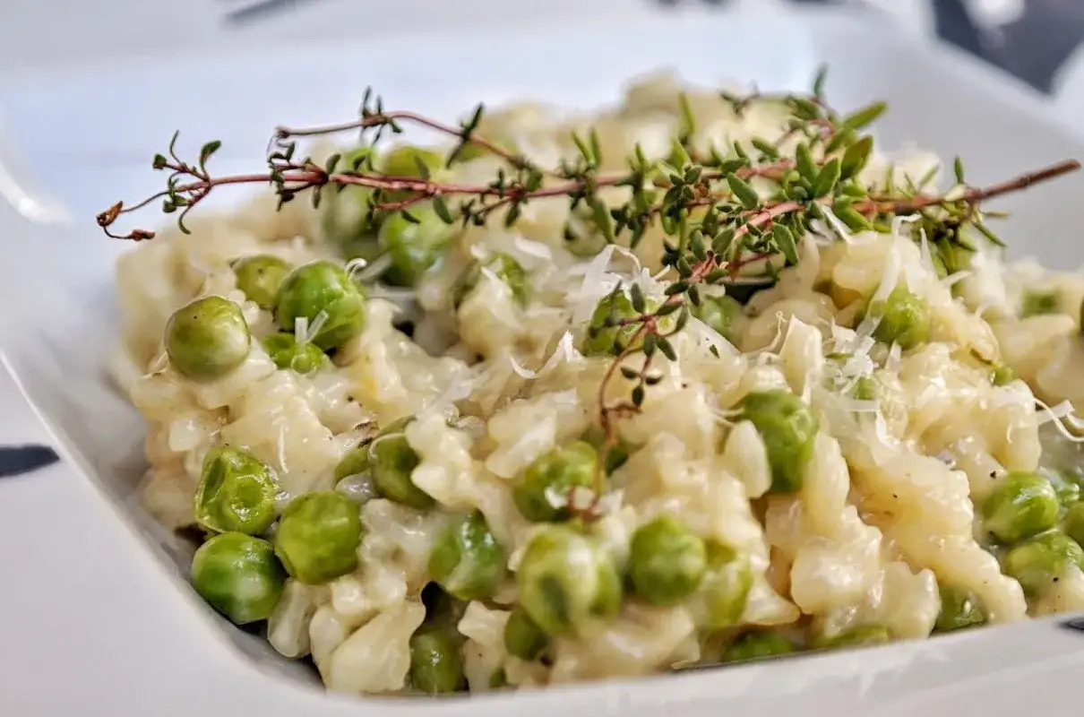 Kremowe risotto z groszkiem, posypane parmezanem i udekorowane gałązką tymianku. Pyszne danie, które zachwyca smakiem.