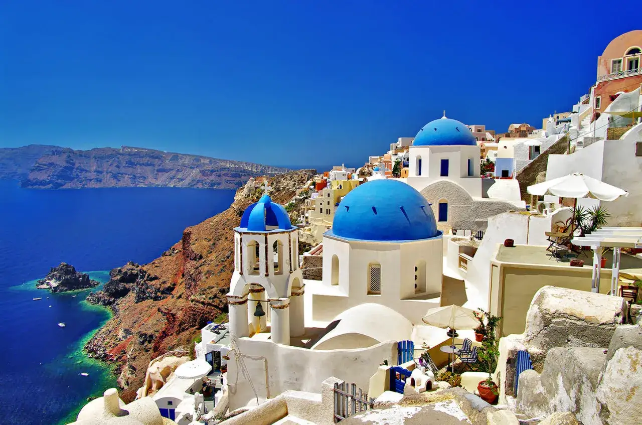 Santorini plaże: białe domy z niebieskimi kopułami na klifie nad turkusowym morzem. Widok zapiera dech w piersiach.