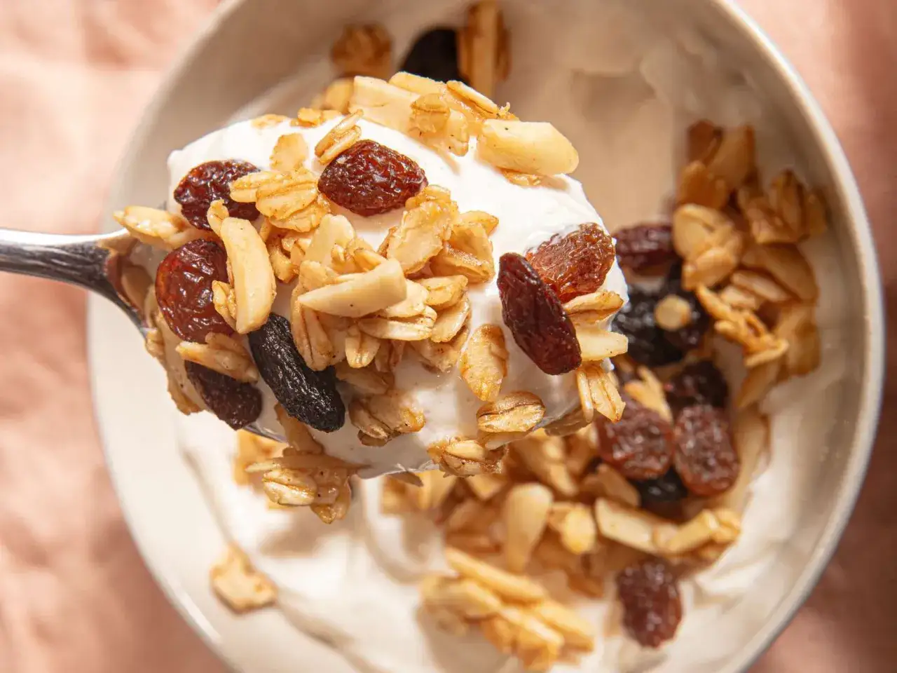 Cuchara llena de yogur con granola casera, pasas y almendras. &iexcl;As&iacute; es como hacer granola deliciosa!