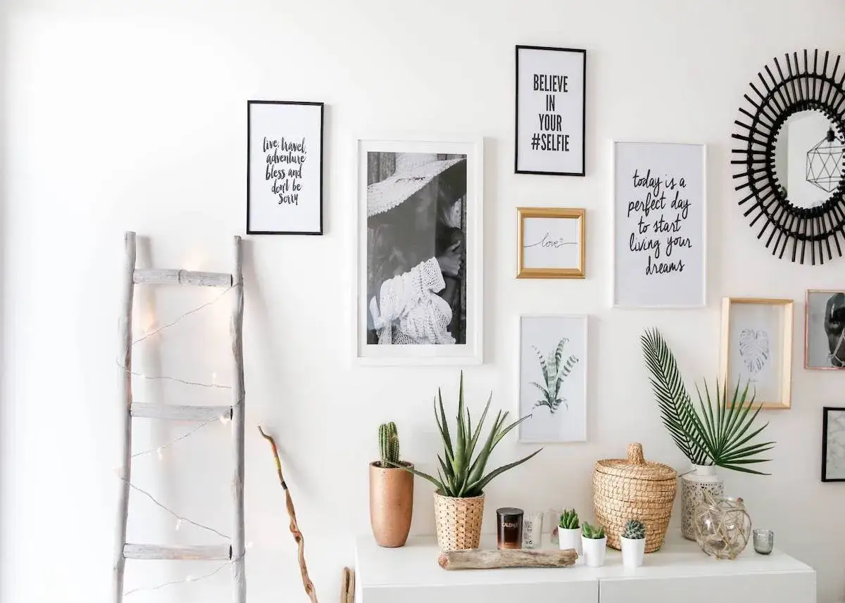 Un mur blanc d&eacute;cor&eacute; avec soin : on peut y admirer plusieurs cadres dispos&eacute;s, des plantes vertes et une &eacute;chelle d&eacute;corative.