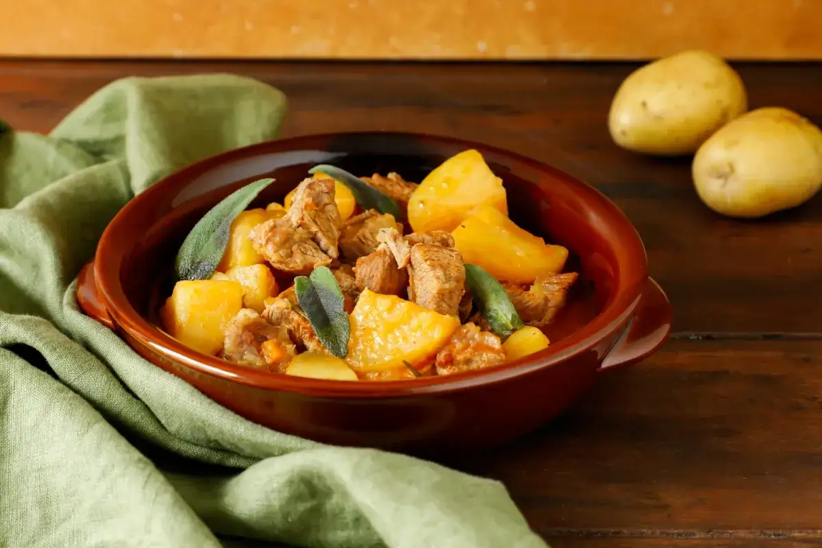 Un saporito spezzatino di vitello con patate e foglie di salvia in una ciotola di terracotta.