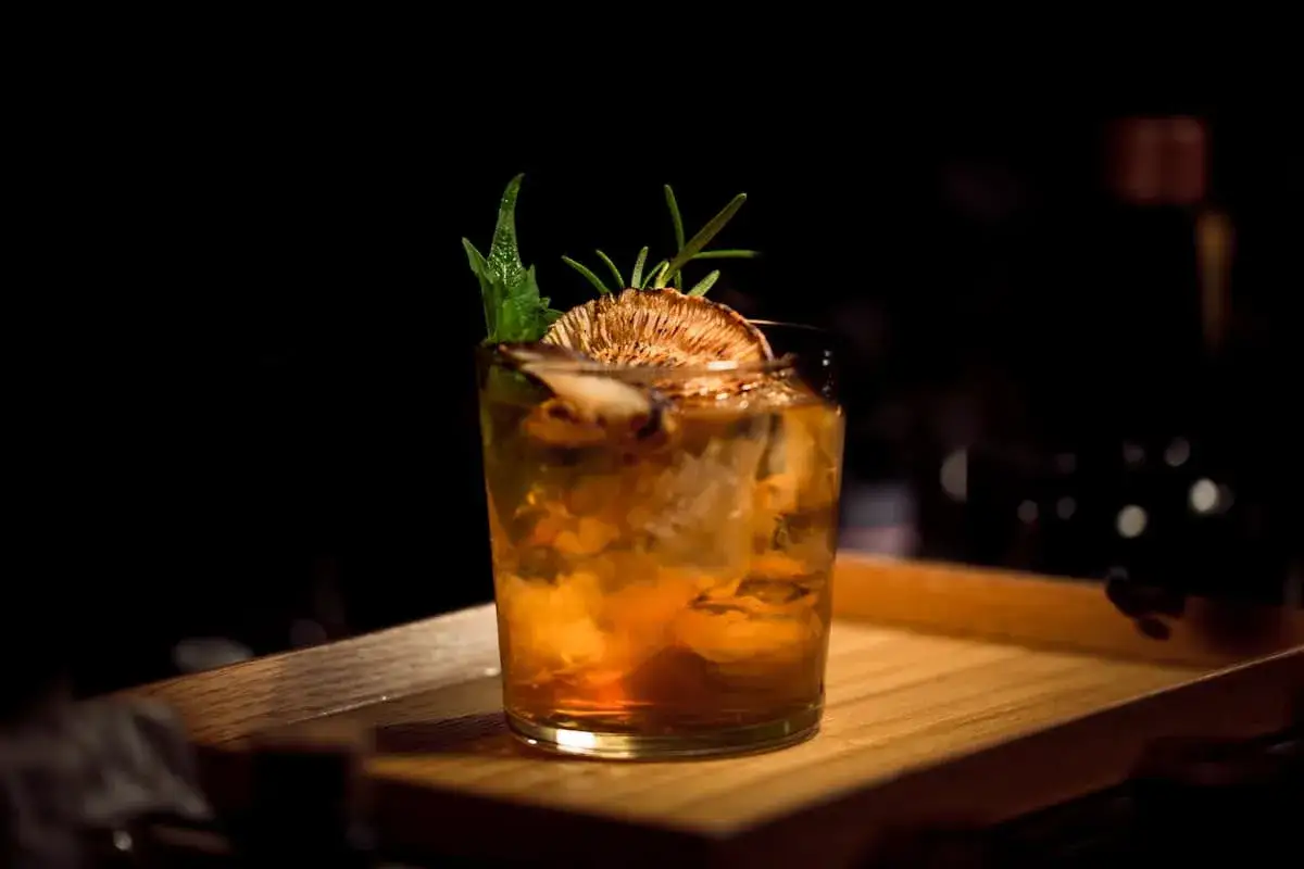 Cocktail ambrato con ghiaccio, guarnito con una fetta di agrume disidratato e rosmarino. Perfetto per un aperitivo Milano Marittima.