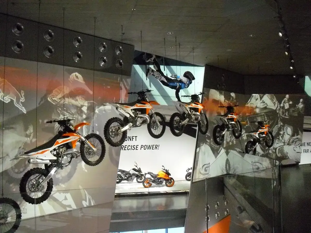 Allestimento dinamico al ktm motohall: moto sospese in aria, un pilota in acrobazia e grafiche suggestive creano un'esperienza immersiva.