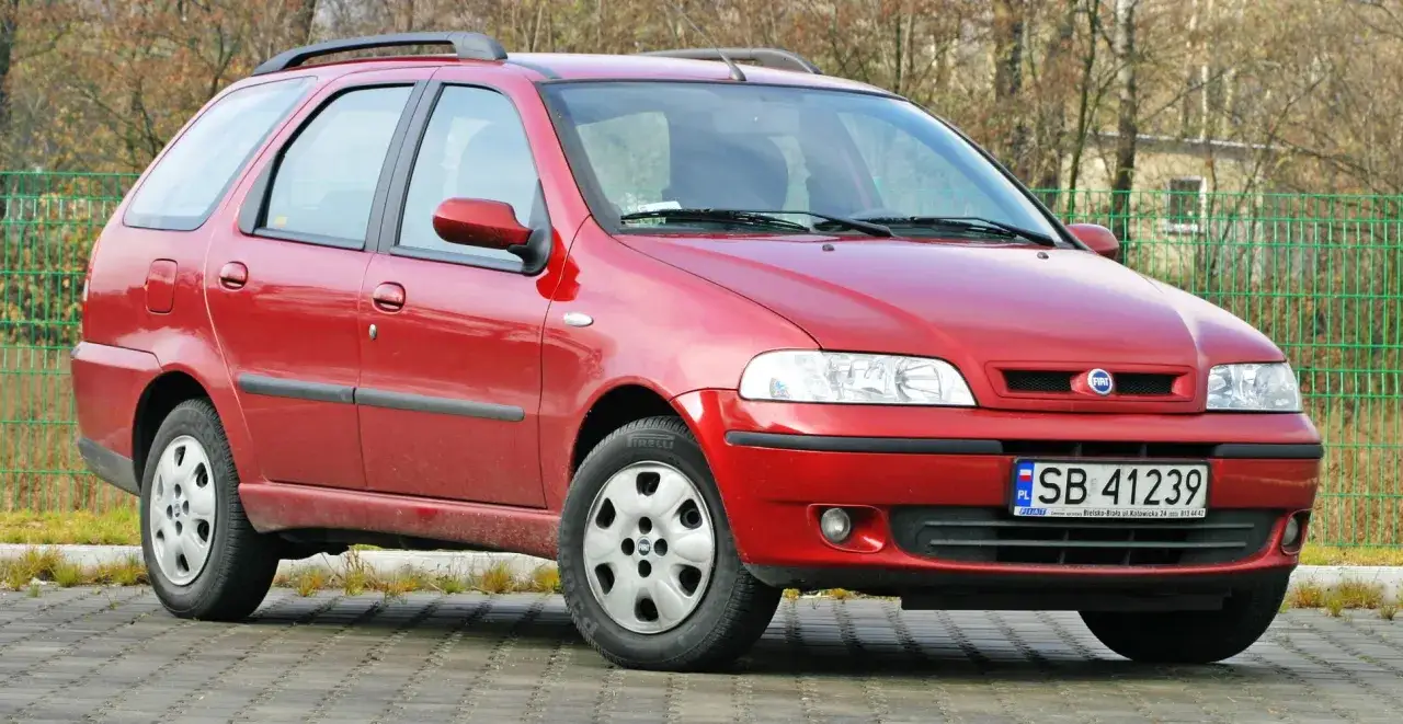 Czerwony Fiat Palio Weekend, jeden z najmniej awaryjnych aut 15 letnich, zaparkowany na kostce brukowej.