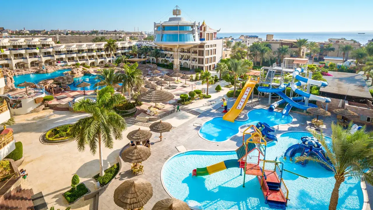 Słoneczny resort Seagull z basenami i zjeżdżalniami wodnymi, otoczony palmami i budynkami hotelowymi, w oddali widać morze.