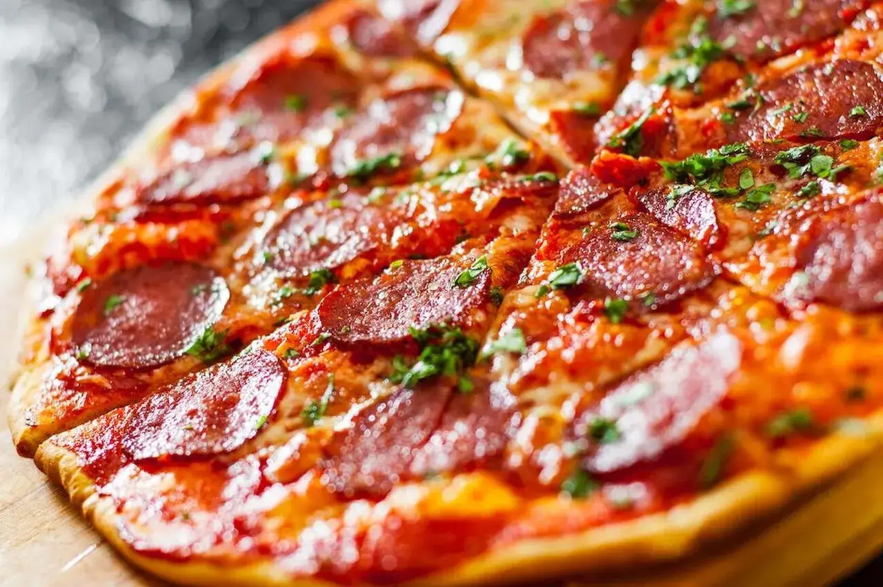 Pyszna pizza pepperoni, z chrupiącym ciastem, które mogło być przygotowane z dodatkiem proszku do pieczenia, posypana świeżą natką pietruszki.