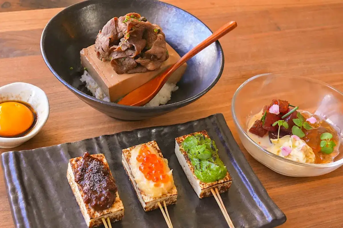 Three skewers of grilled tofu, each with a different topping, showcase creative tofu recipes. One has a dark sauce, another ikura and mashed potato, and the third a vibrant green puree.