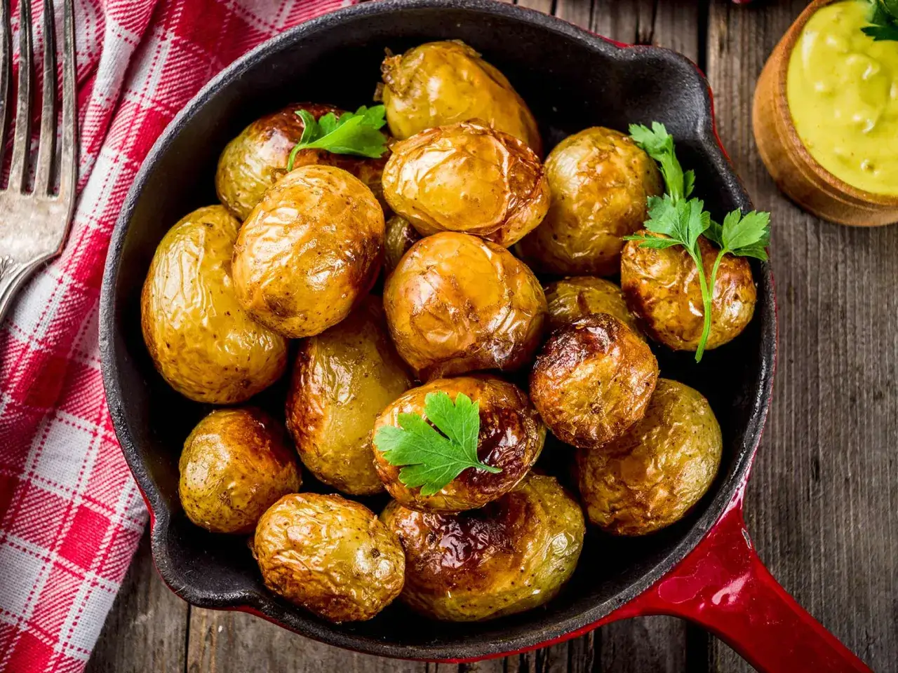 Pommes de terre grenaille au four, dorées et croustillantes, garnies de persil frais, servies dans une poêle rouge.
