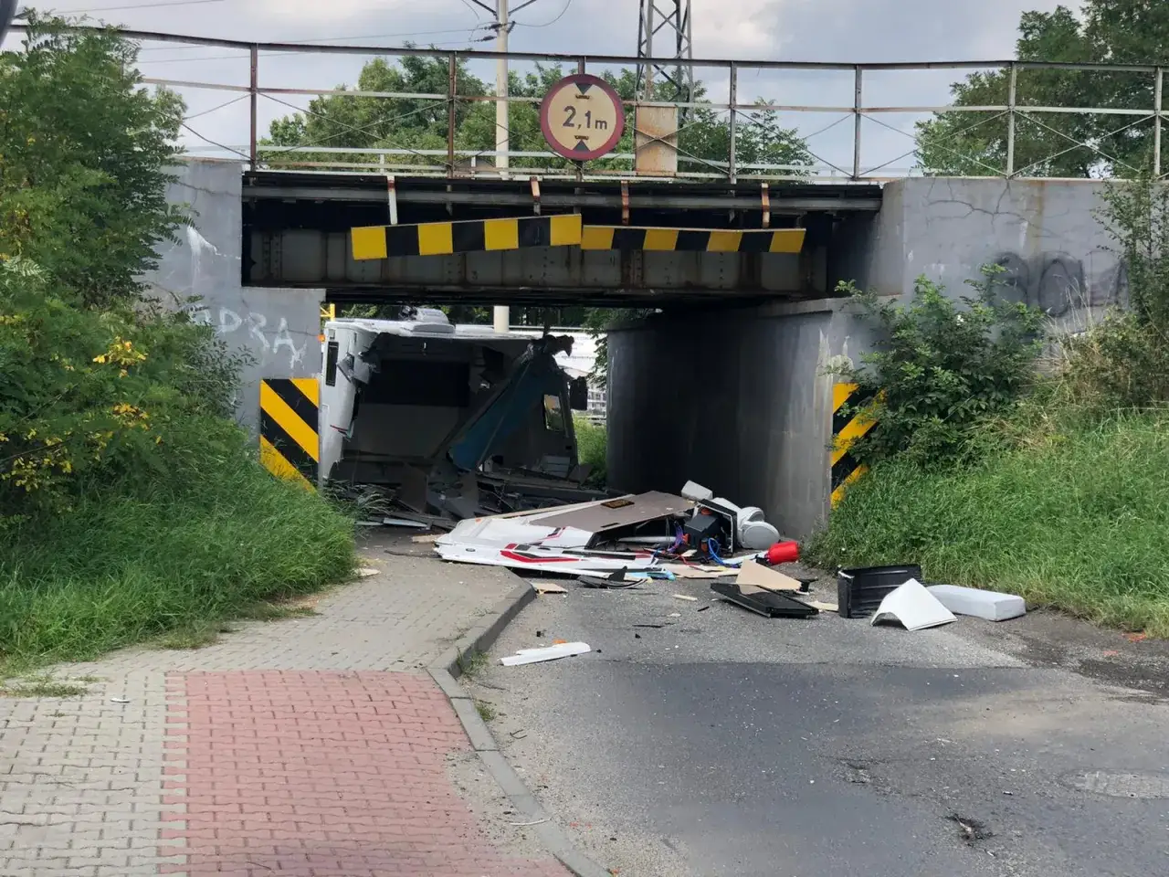 Kamper uderzył w wiadukt, ignorując znak o ograniczeniu wysokości 2,1m. Pojazd jest zniszczony, a jego wnętrze rozsypane.