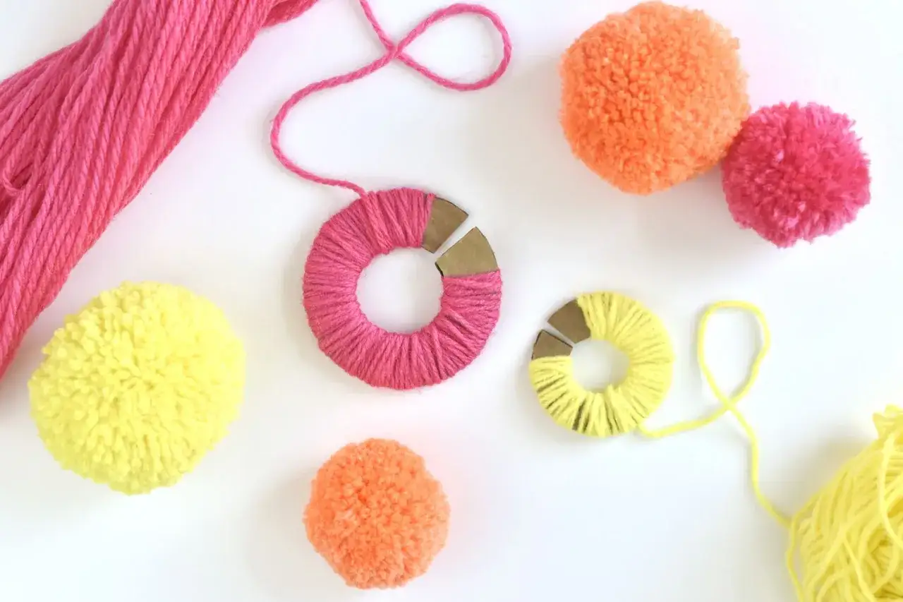 Kolorowe pompony DIY w trakcie tworzenia. Włóczki i kartonowe szablony do nawijania.