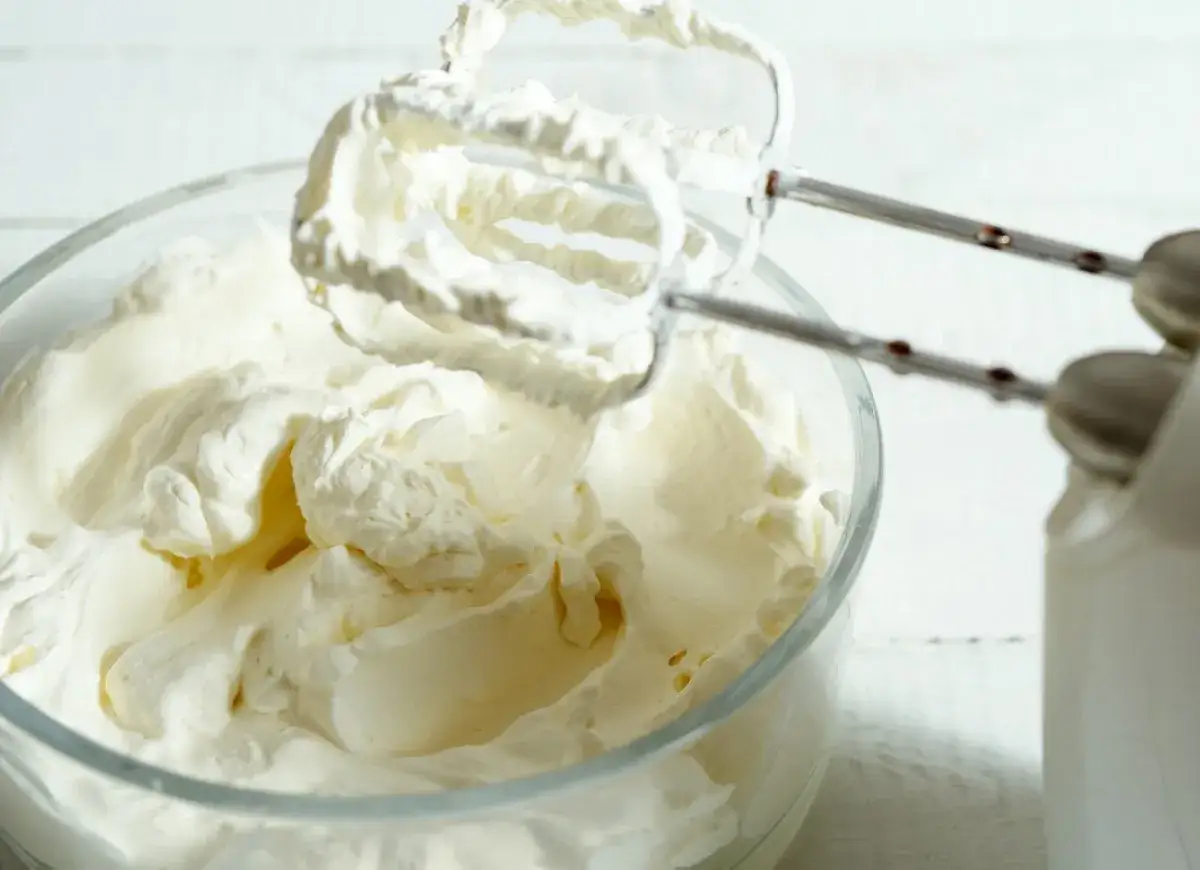 Mieszadła miksera ubijają puszysty, prosty krem z mascarpone bez śmietany w szklanej misce.