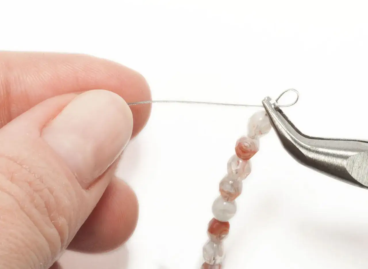 Mano sujetando hilo metálico para collares. Se usa pinza para crear un bucle, demostrando cuál es el mejor hilo para hacer collares.