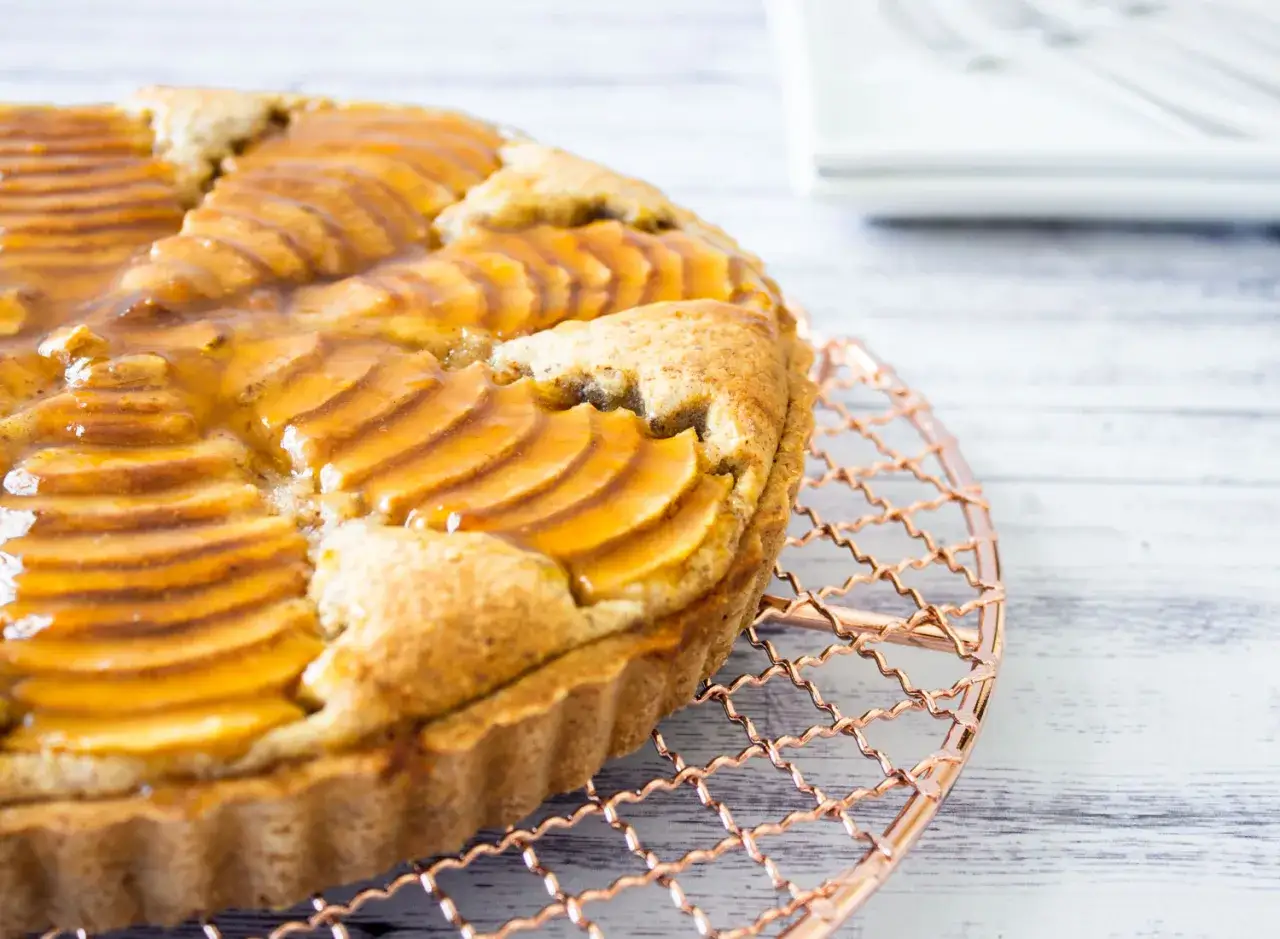Deliciosa tarta de pera francesa con láminas de pera caramelizadas sobre una base dorada, enfriándose en una rejilla de cobre.