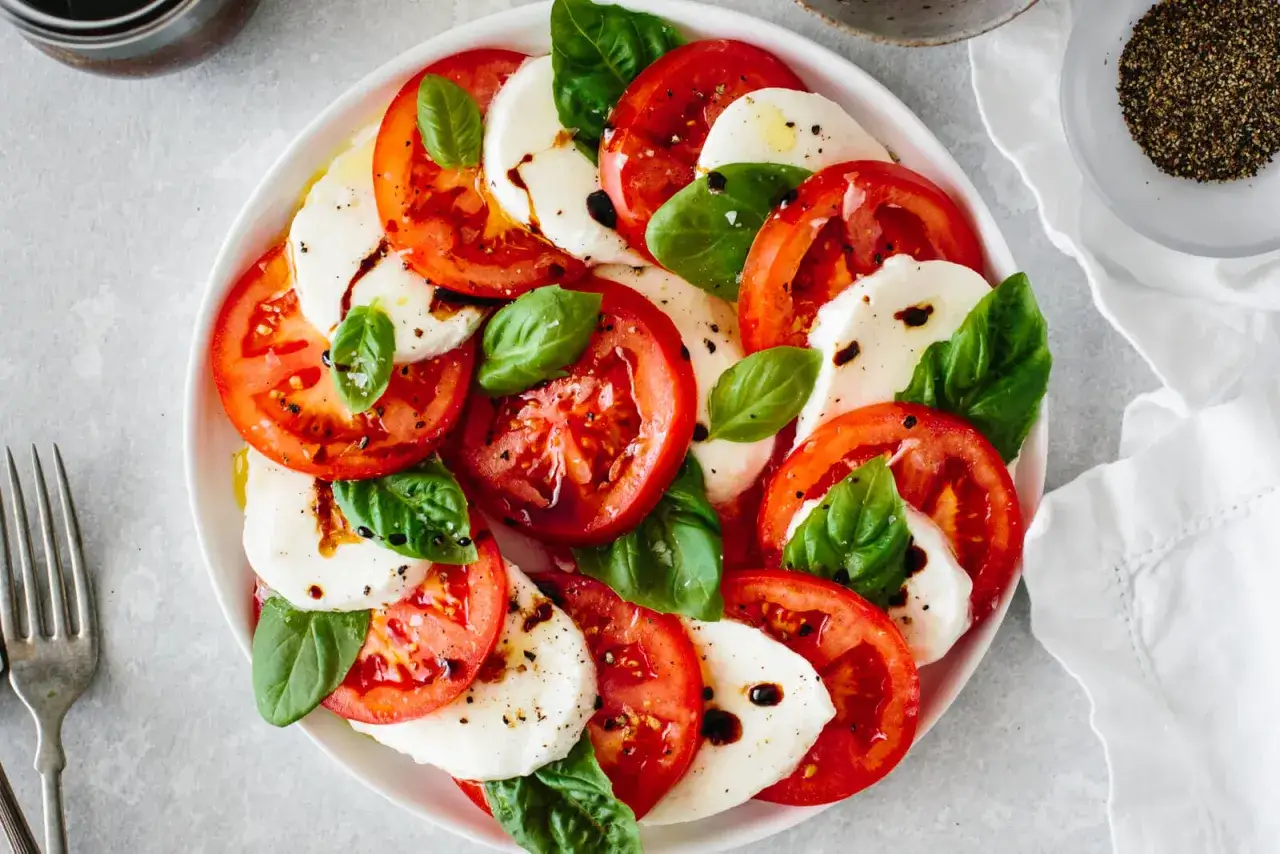 Una refrescante ensalada caprese con rodajas de tomate y mozzarella fresca, aderezada con albahaca y glaseado balsámico.