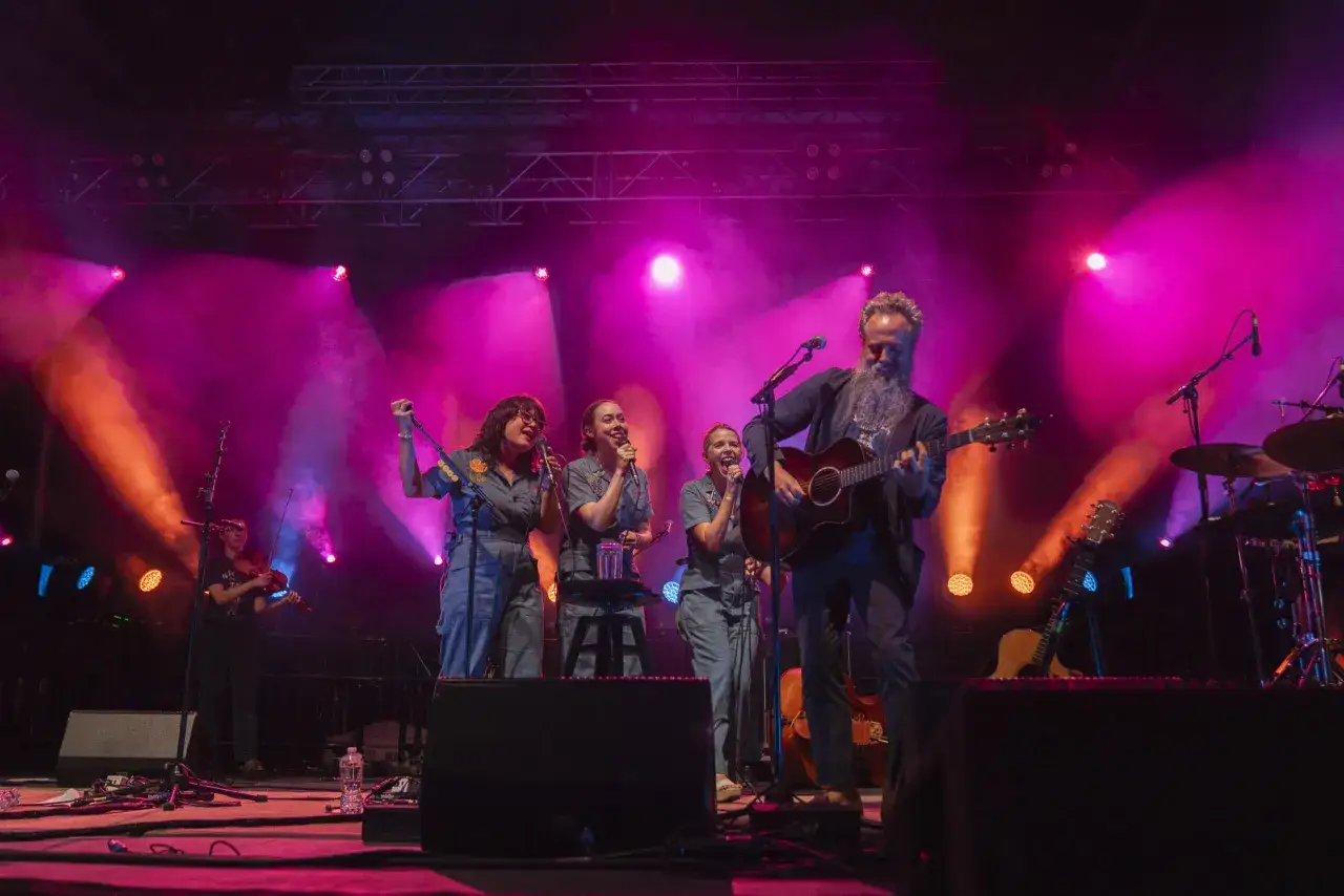 Zespół muzyczny na scenie, w różowych światłach. Mężczyzna gra na gitarze, kobiety śpiewają. To może być ich ostatnia wspólna impreza.