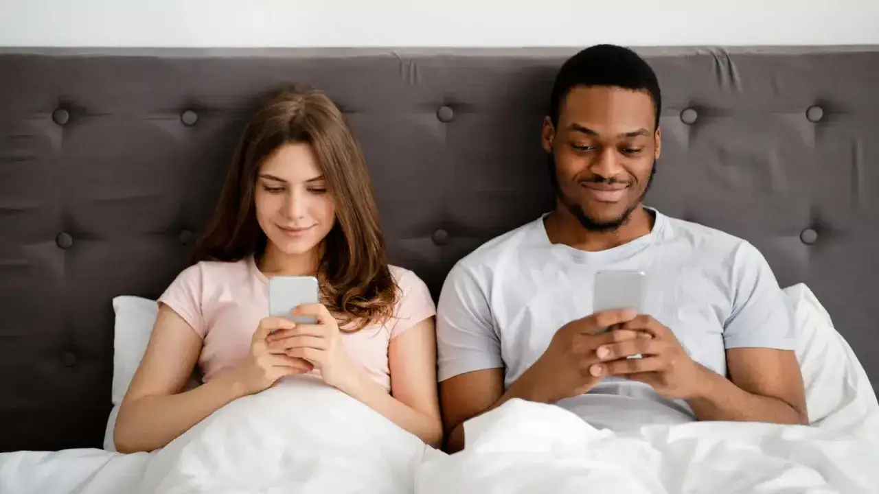 Coppia a letto, ognuno col proprio smartphone. Un esempio di phubbing, ignorare il partner per il telefono.