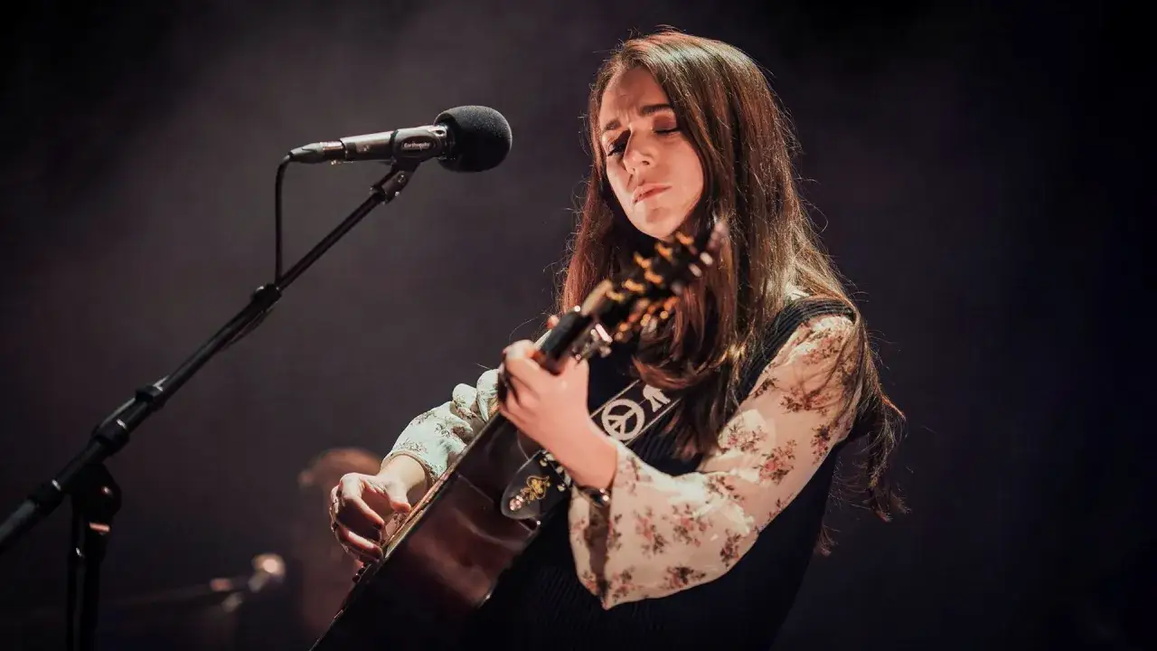 Melissa Horn, med slutna ögon, spelar gitarr på scenen. En fredssymbol syns på hennes gitarrband.