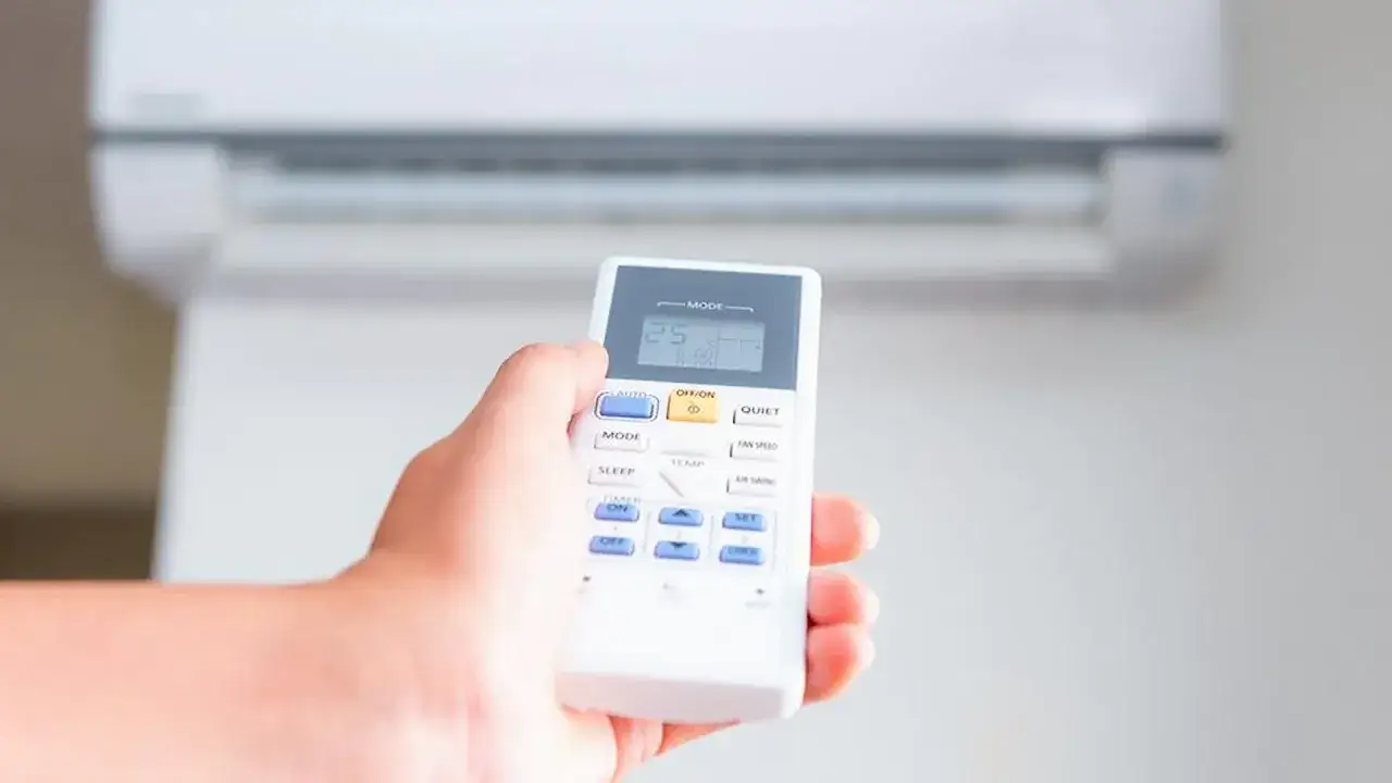 Mano sujetando control remoto para aire acondicionado, ajustando la temperatura a 25 grados para combatir el calor.